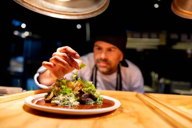 Chef plating and garnishing dishes under warm heat lamps in a restaurant kitchen