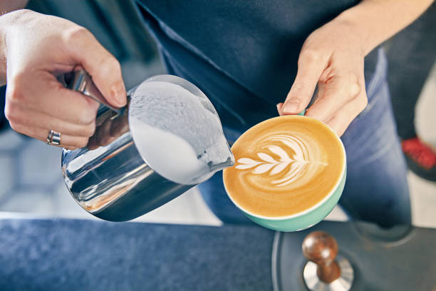 Barista pouring steamed milk into a latte, creating rosetta art in a turquoise cup